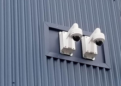 Two dome security cameras installed on exterior metal siding wall.